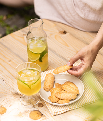 A person sitting in the sun, taking a delicious Croquiet Citron-gingembre, lime and ginger crunchy biscuits, to go with their glass of homemade lime iced tea.