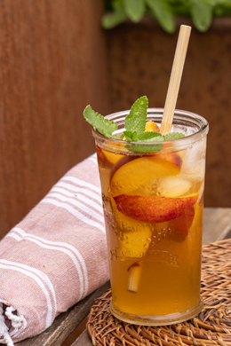 Large transparent glass of iced peaches infusion, decorated with mint.